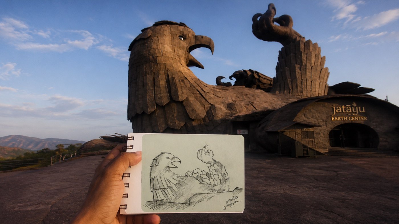 A pencil sketch of the Jatayu Earth Center eagle sculpture, held up in front of the real statue at sunset.